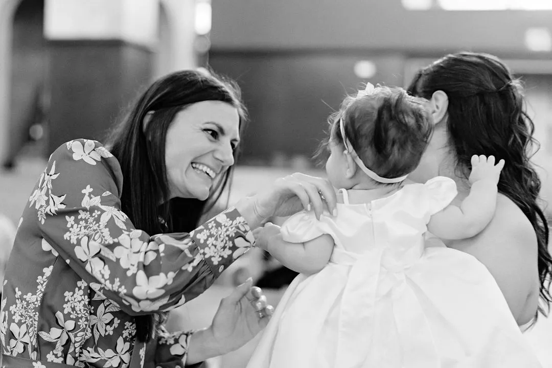 Photo en noir et blanc d'une femme souriante saluant le bébé en robe de baptême