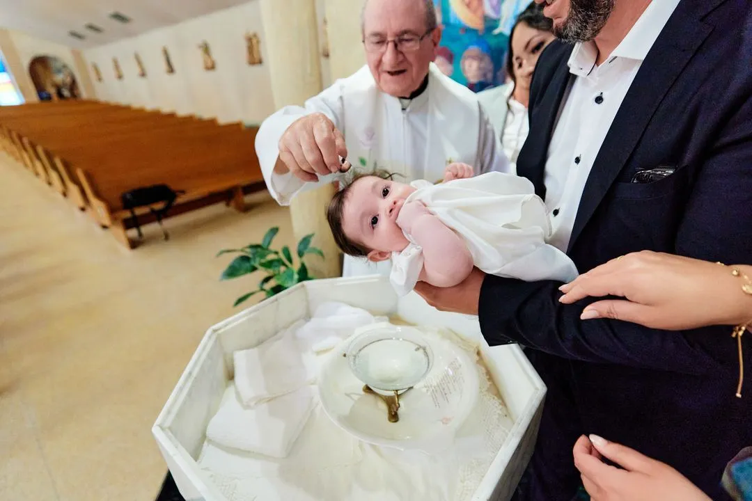Le prêtre verse l'eau bénite sur le bébé aux fonts baptismaux