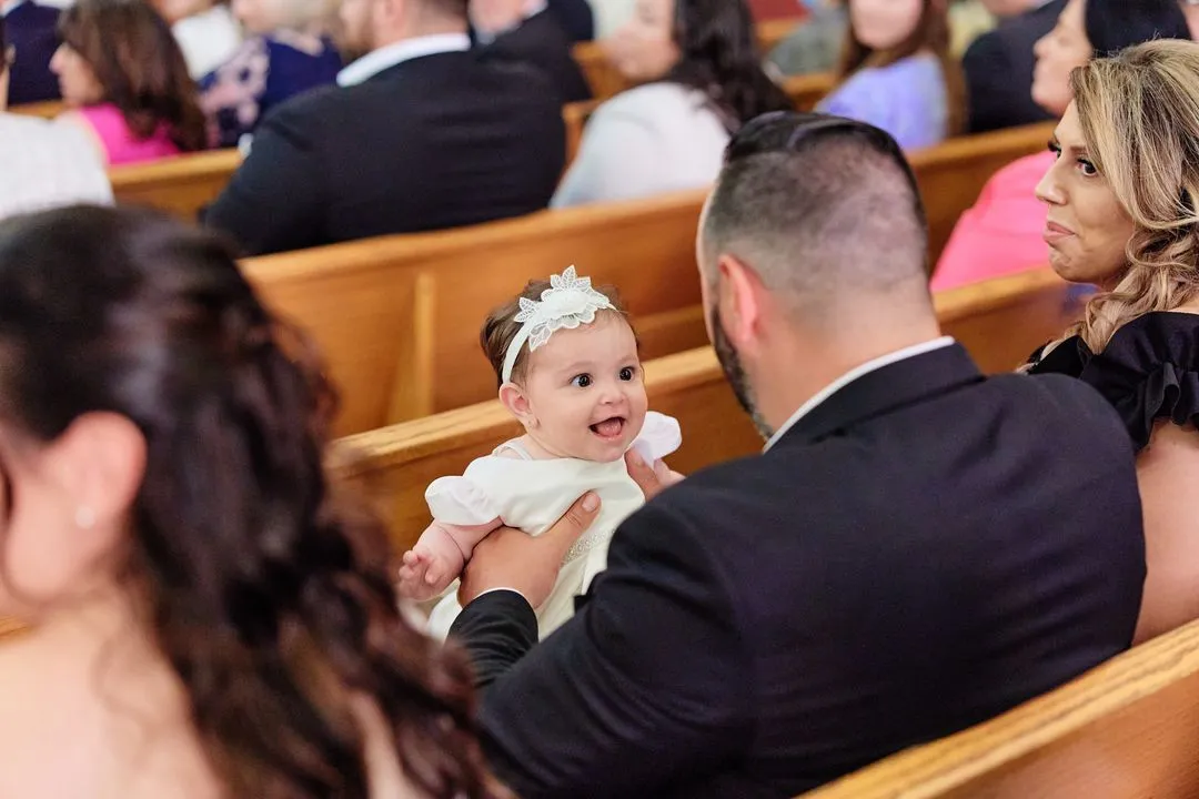 Bébé souriant en robe blanche tenu dans les bancs de l'église pendant le baptême