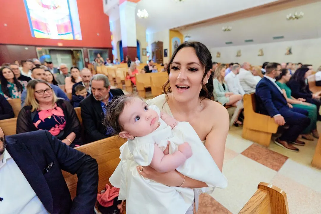 Une femme tient le bébé en robe de baptême pendant que les invités regardent depuis les bancs de l'église