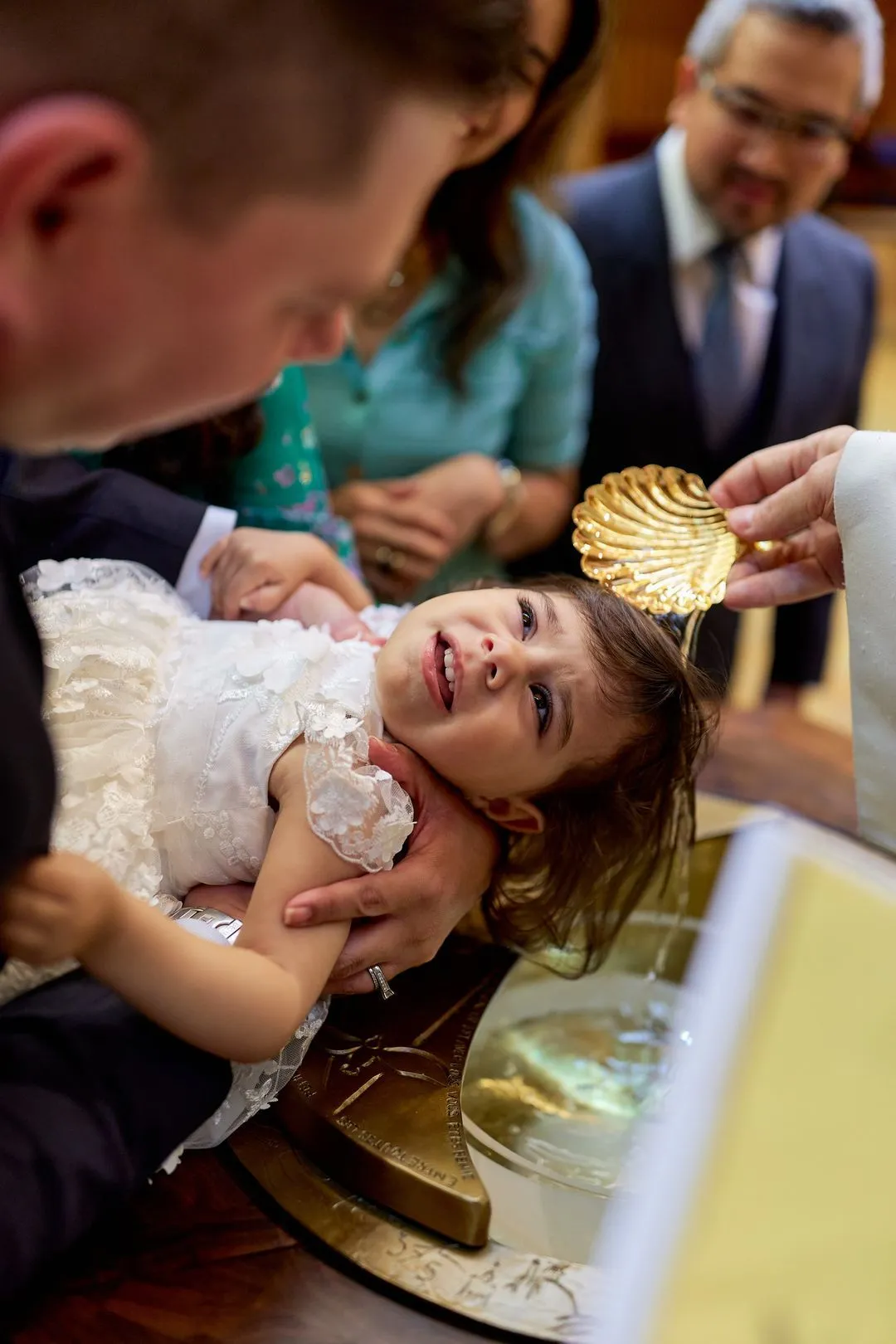 Le prêtre verse l'eau baptismale avec une coquille dorée sur la tête d'une fillette