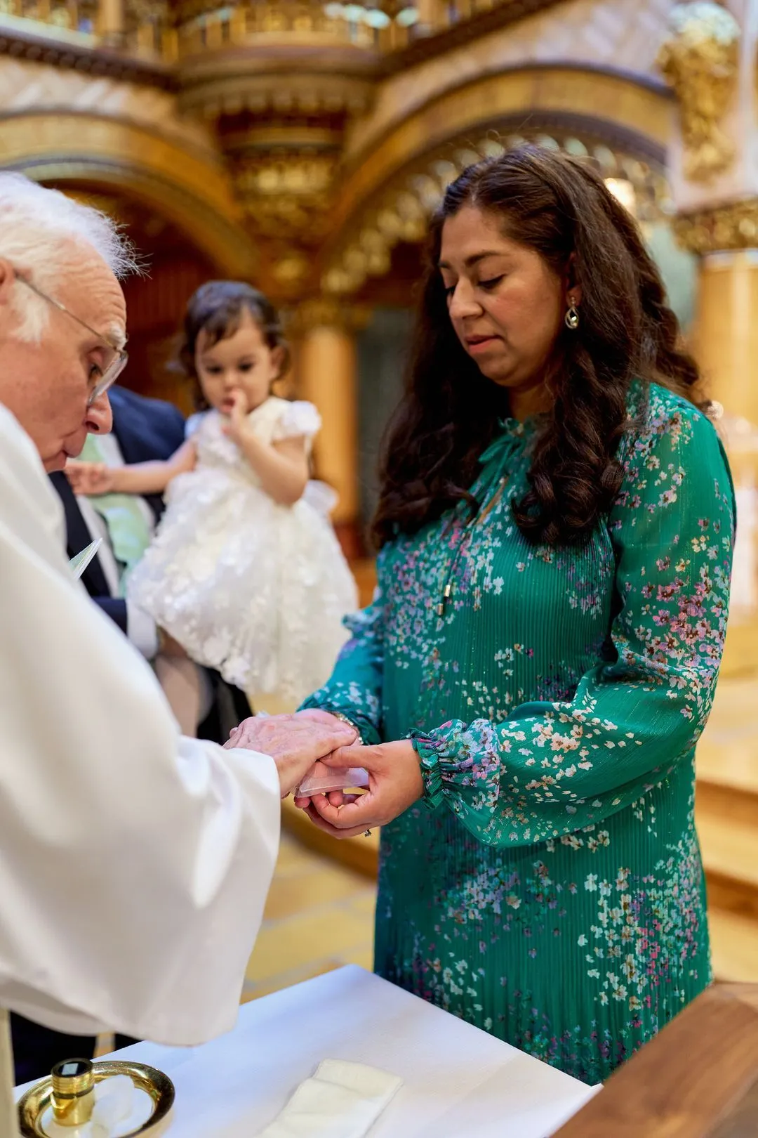 Le prêtre tient les mains d'une femme pendant le baptême d'une fillette dans une chapelle ornée
