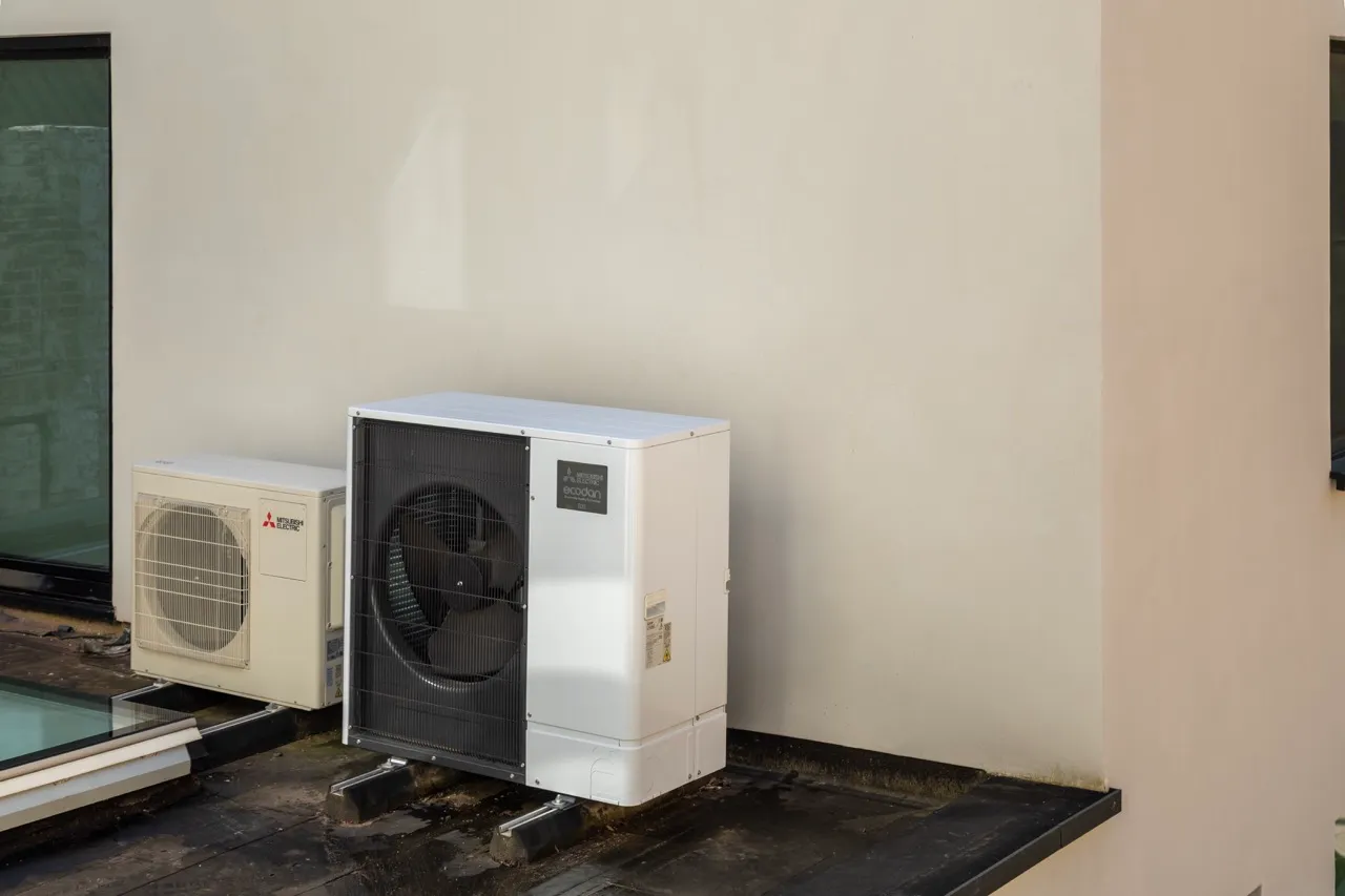Two white outdoor heatpump units mounted on a flat rooftop against a beige wall.