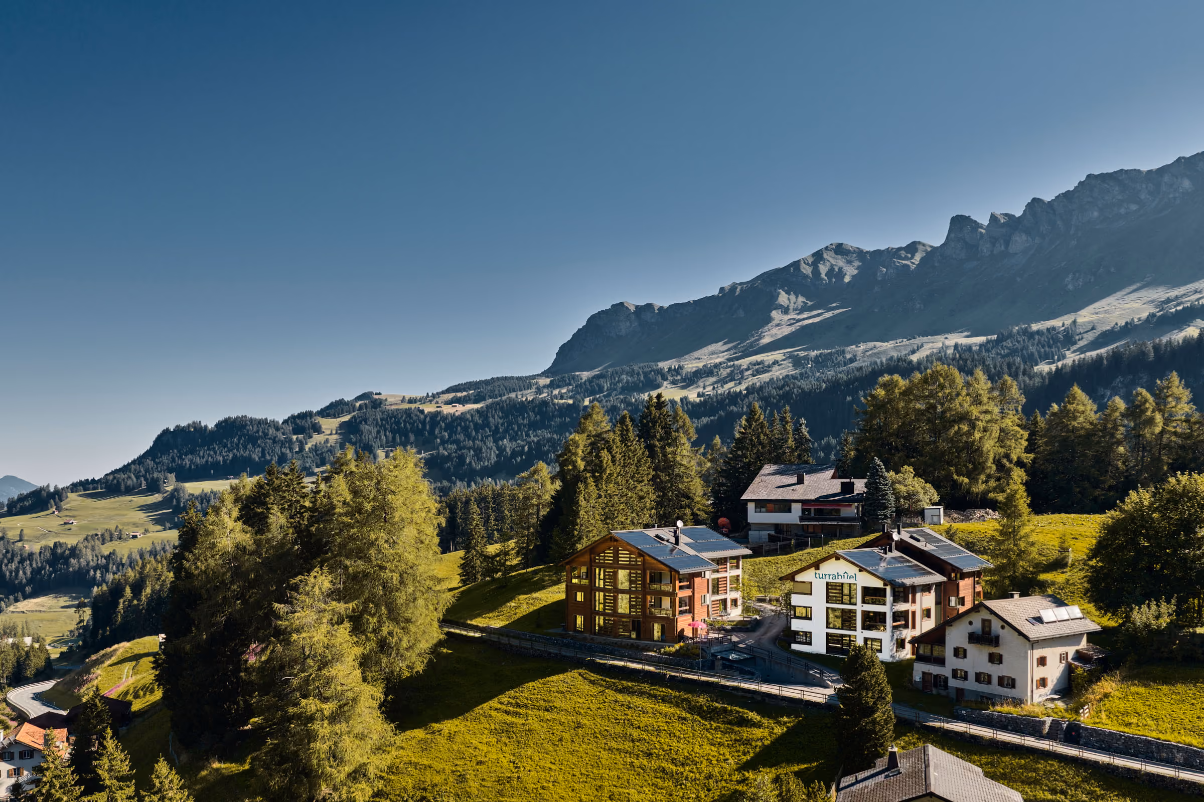 Blick auf die zwei Häuser der Turrabuel Ferienwohnungen in Lenzerheide eingebettet in die malerische Bergwelt im Sommer