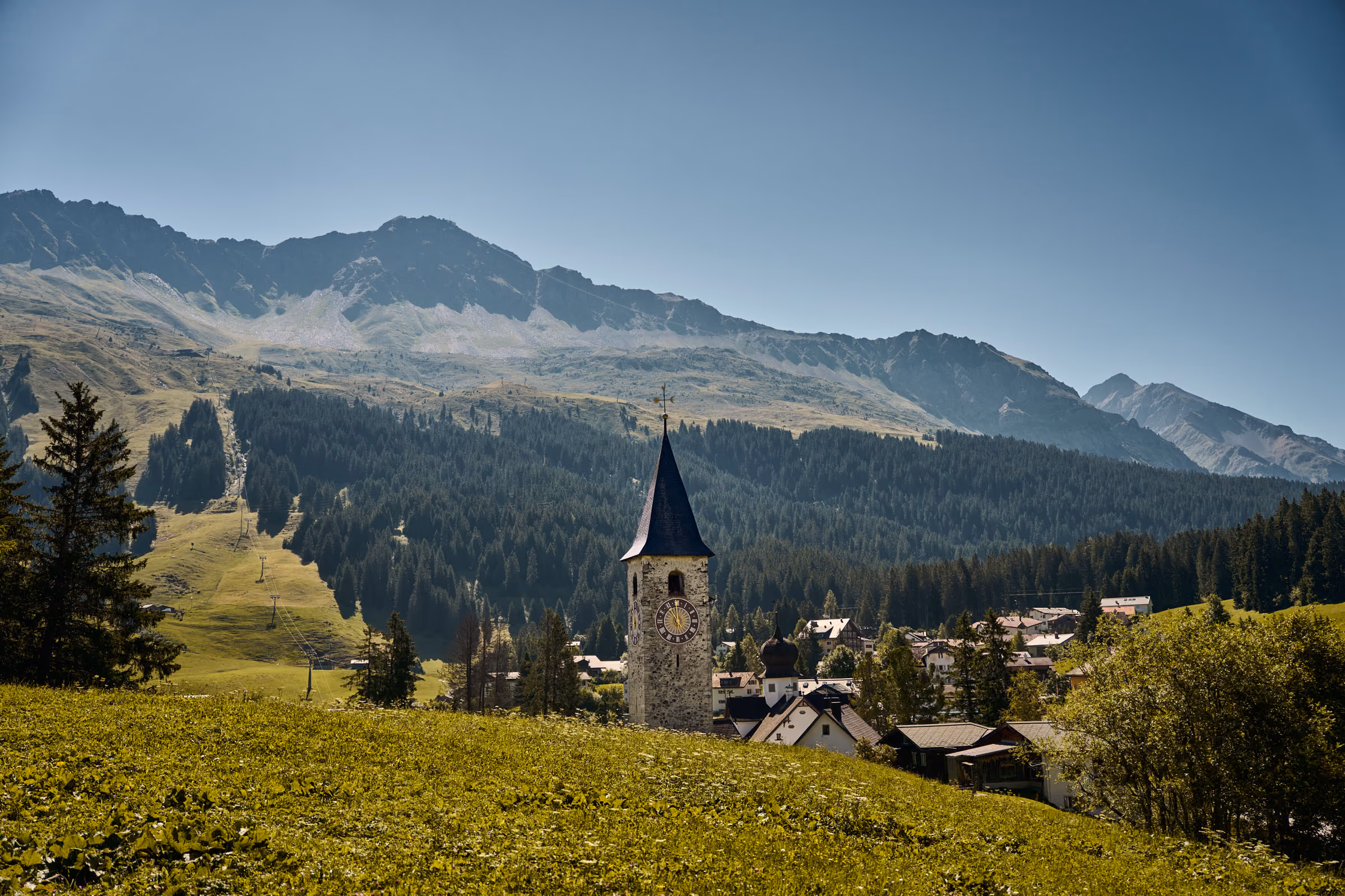 Der Parpaner Kichturm in grüner Sommerlandschaft ist Teil der Namensgebung unserer Ferienwohnungen in Lenzerheide.  