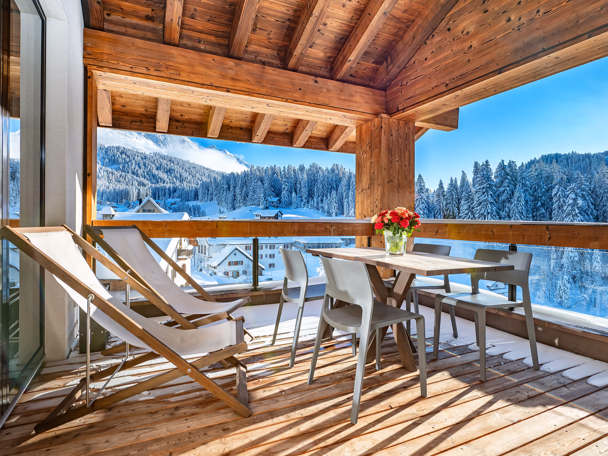 Die Aussicht auf verschneite Wälder und Berge bei Sonnenschein vom Balkon einer der Turrabuel Ferienwohnungen in Lenzerheide