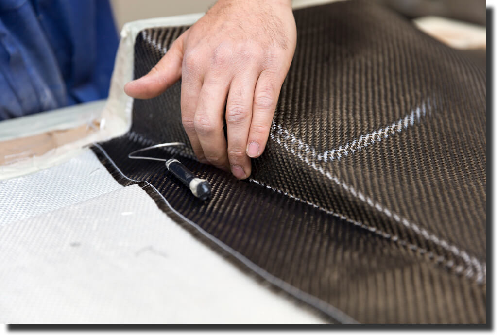 Shop floor lay‑up: carbon‑fiber layer positioned over white fiberglass mat – visualizing fiberglass vs carbon fiber strength in hybrid builds.