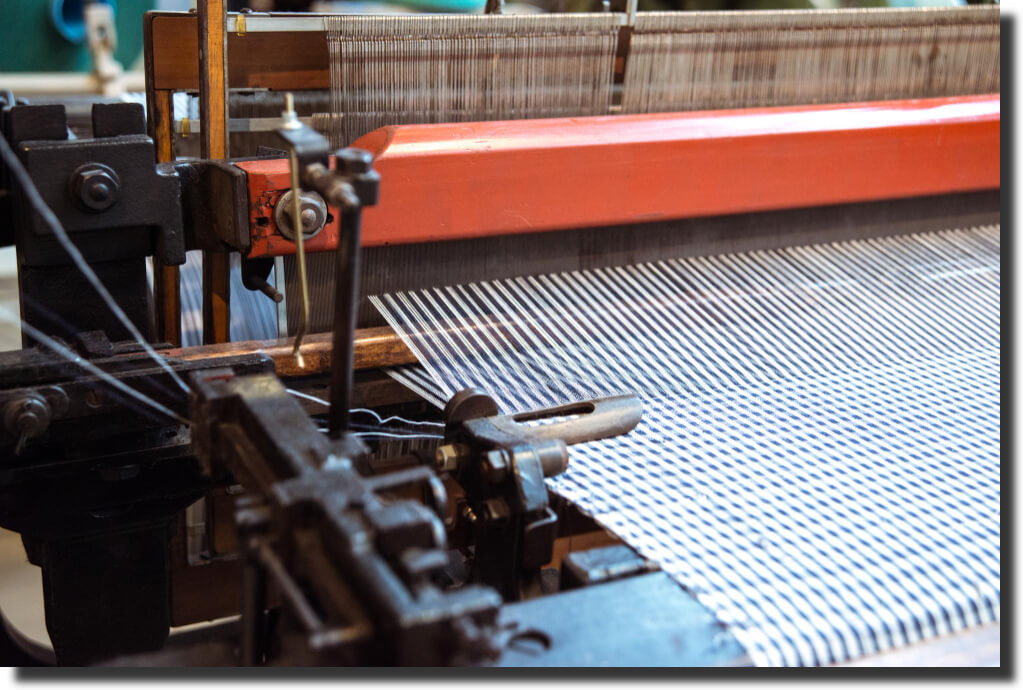 Industrial loom weaving fiberglass fabric for composites, capturing manufacturing contrast in the fiberglass vs carbon fiber debate.