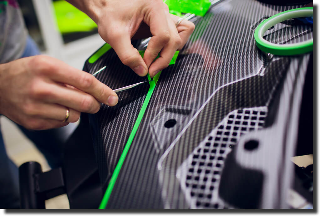 Close‑up trimming carbon‑fiber bodywork while adding green film; showcases precision handling where is fiberglass stronger than carbon fiber is tested.