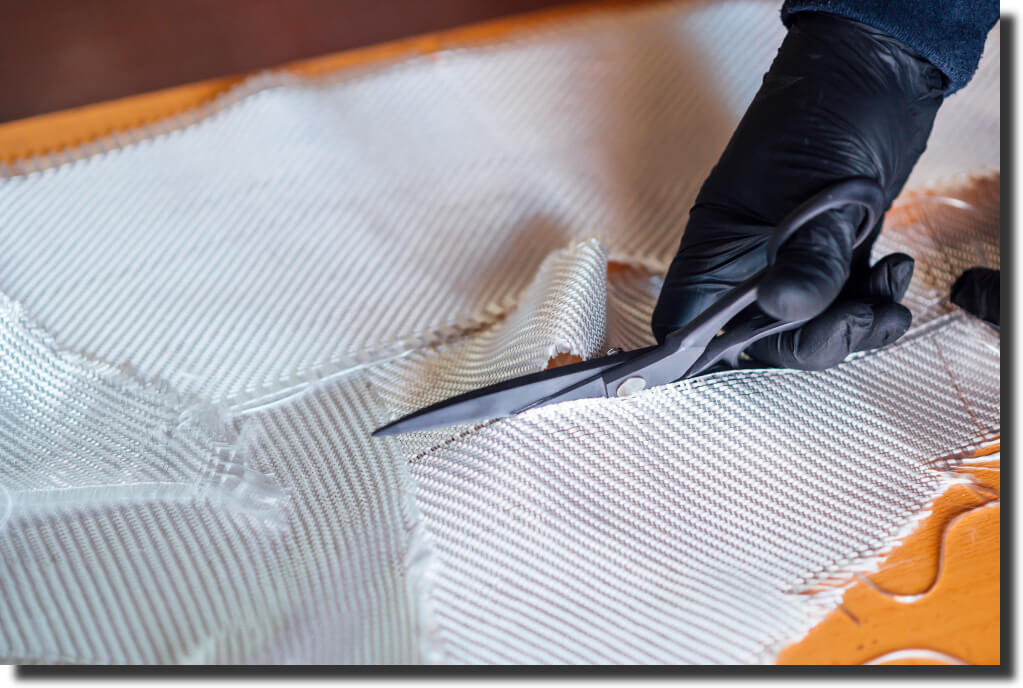Gloved tech cutting fiberglass/Kevlar cloth; prep step in composite tooling, sizing materials before layup and cure.