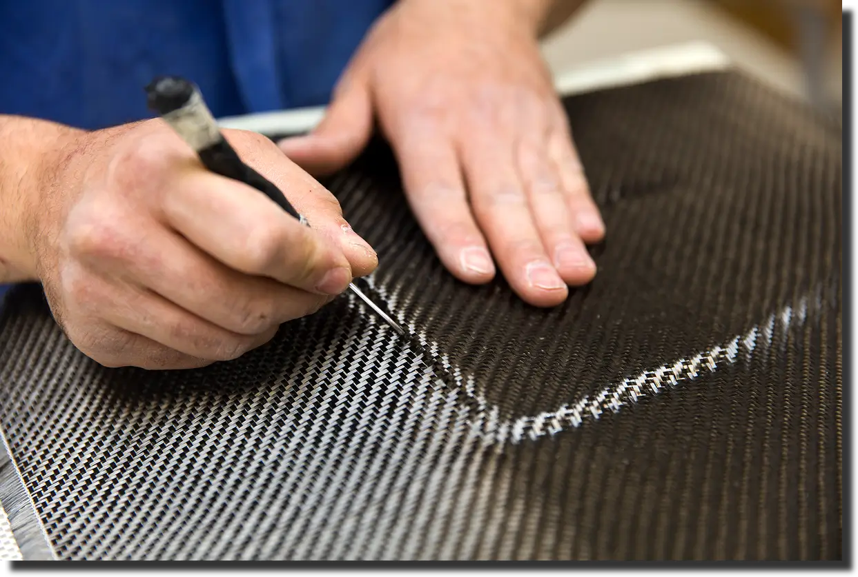 Engineer marking a carbon fiber laminate during layup, connecting design choices to carbon fiber elastic modulus and part-level stiffness.