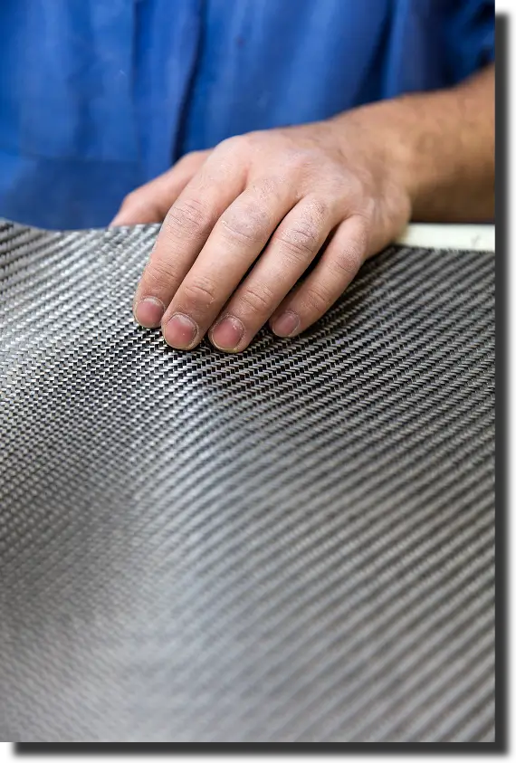 Gloved technician cutting carbon fiber fabric, where layup and trimming influence the modulus of elasticity of carbon fiber in real parts.