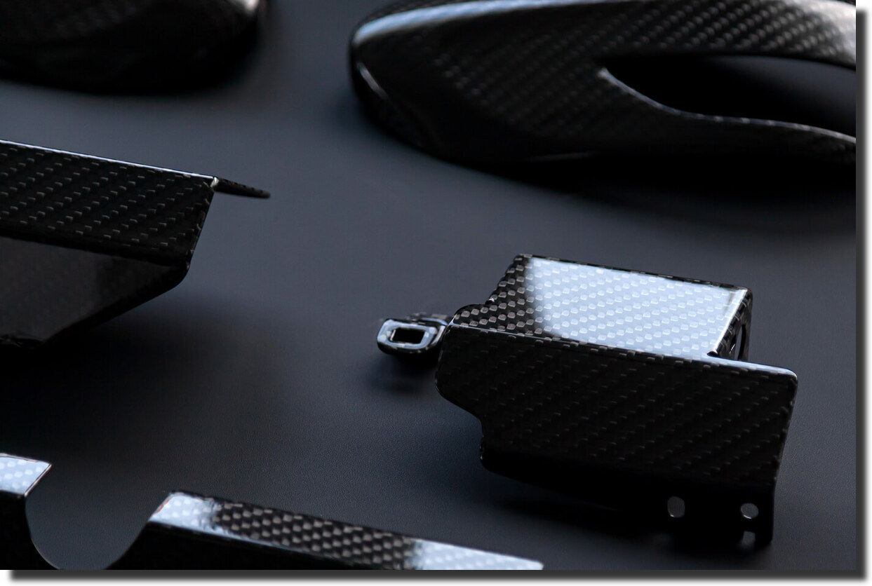 Detail of sports car body made from real carbon fiber, showing reflections on a structural panel not a fake carbon fiber wrap