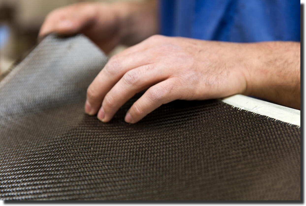 Hands holding a sheet of real carbon fiber fabric, showing structural reinforcement texture beyond fake carbon fiber skins