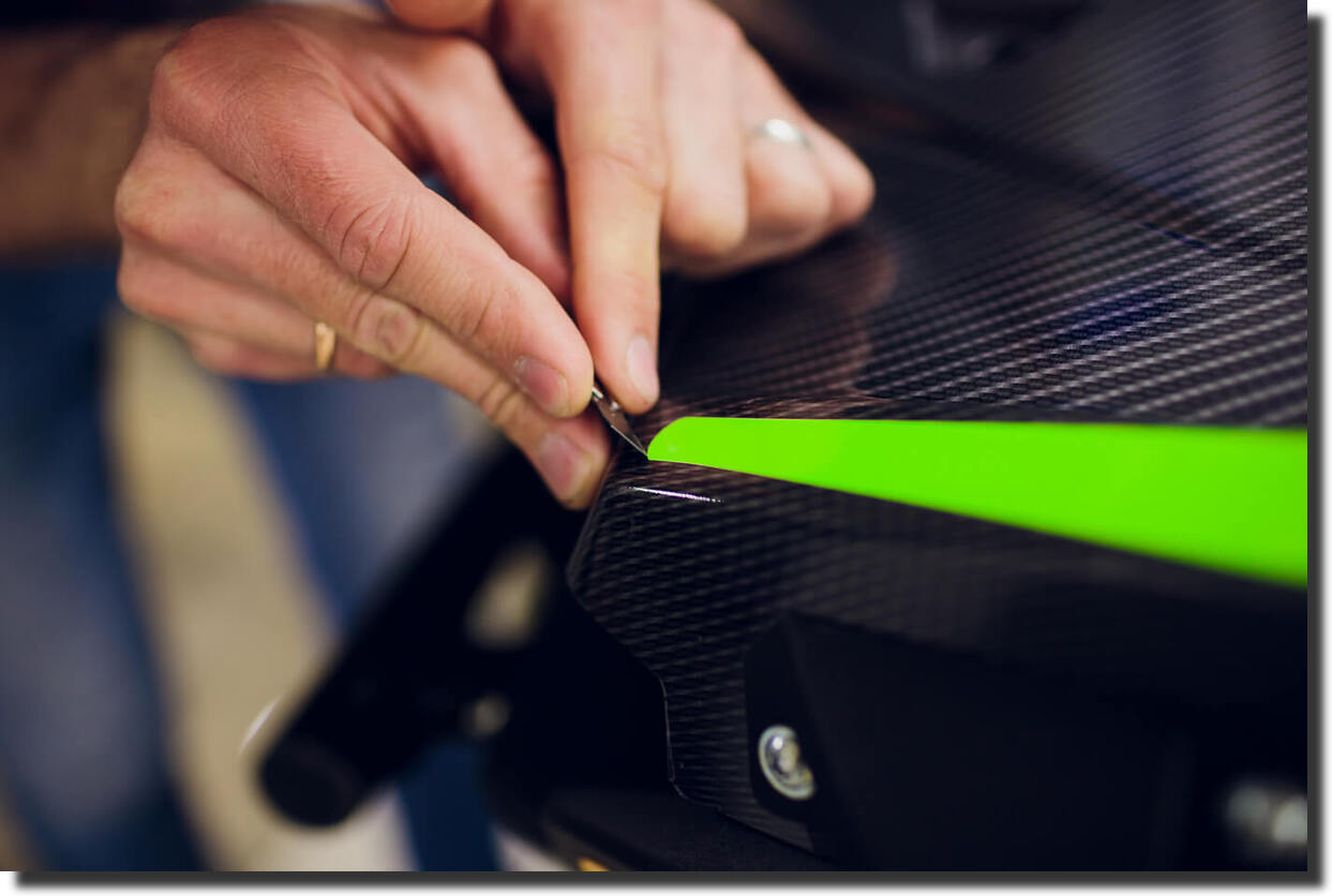 Technician applying vinyl wrap over a panel, representing a fake carbon fiber look versus real carbon fiber composite parts