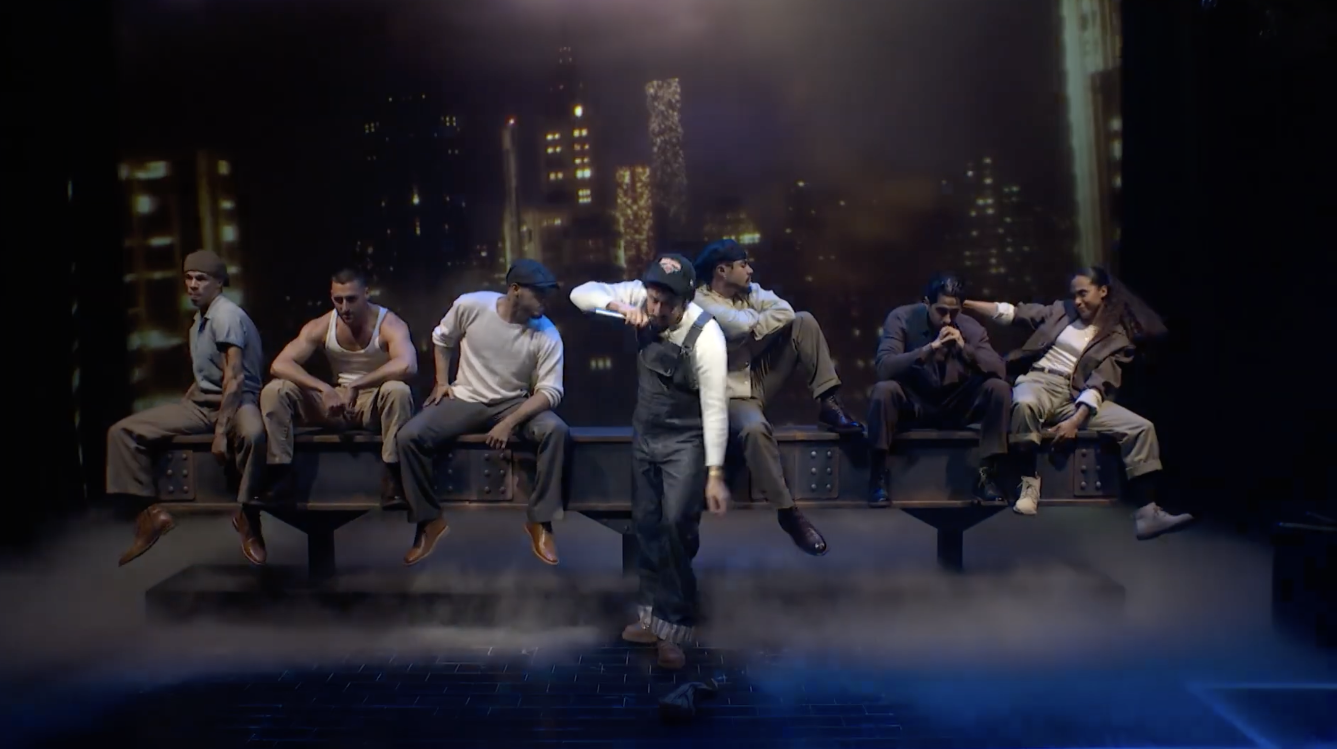 Dance performance with group of men on stage with city skyline backdrop
