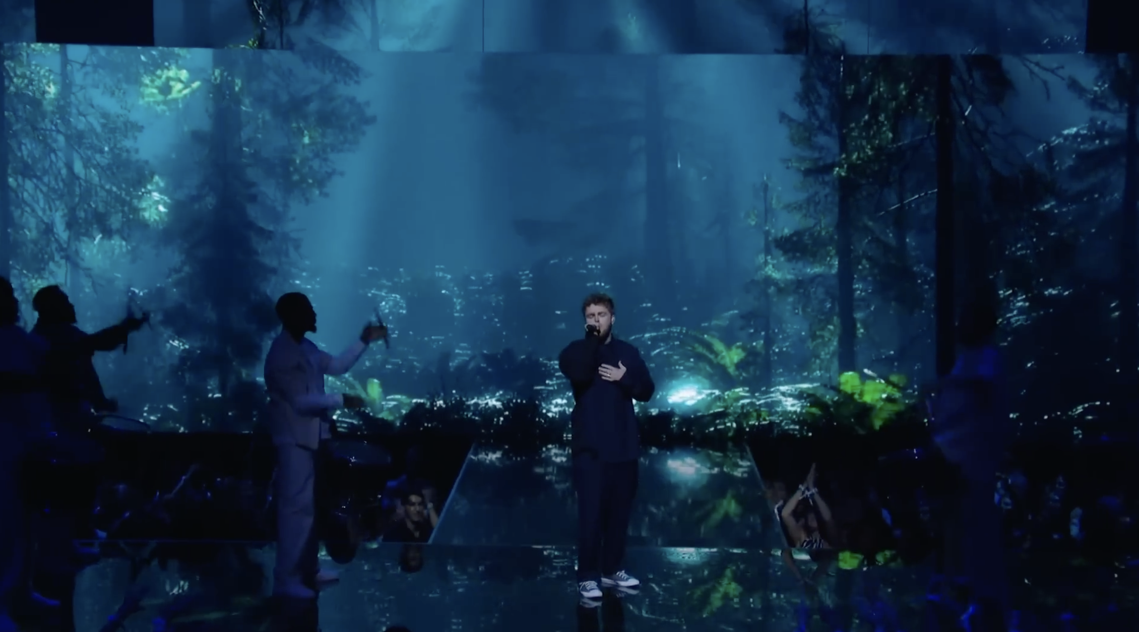 Singer performing on stage with misty forest and dramatic blue lighting