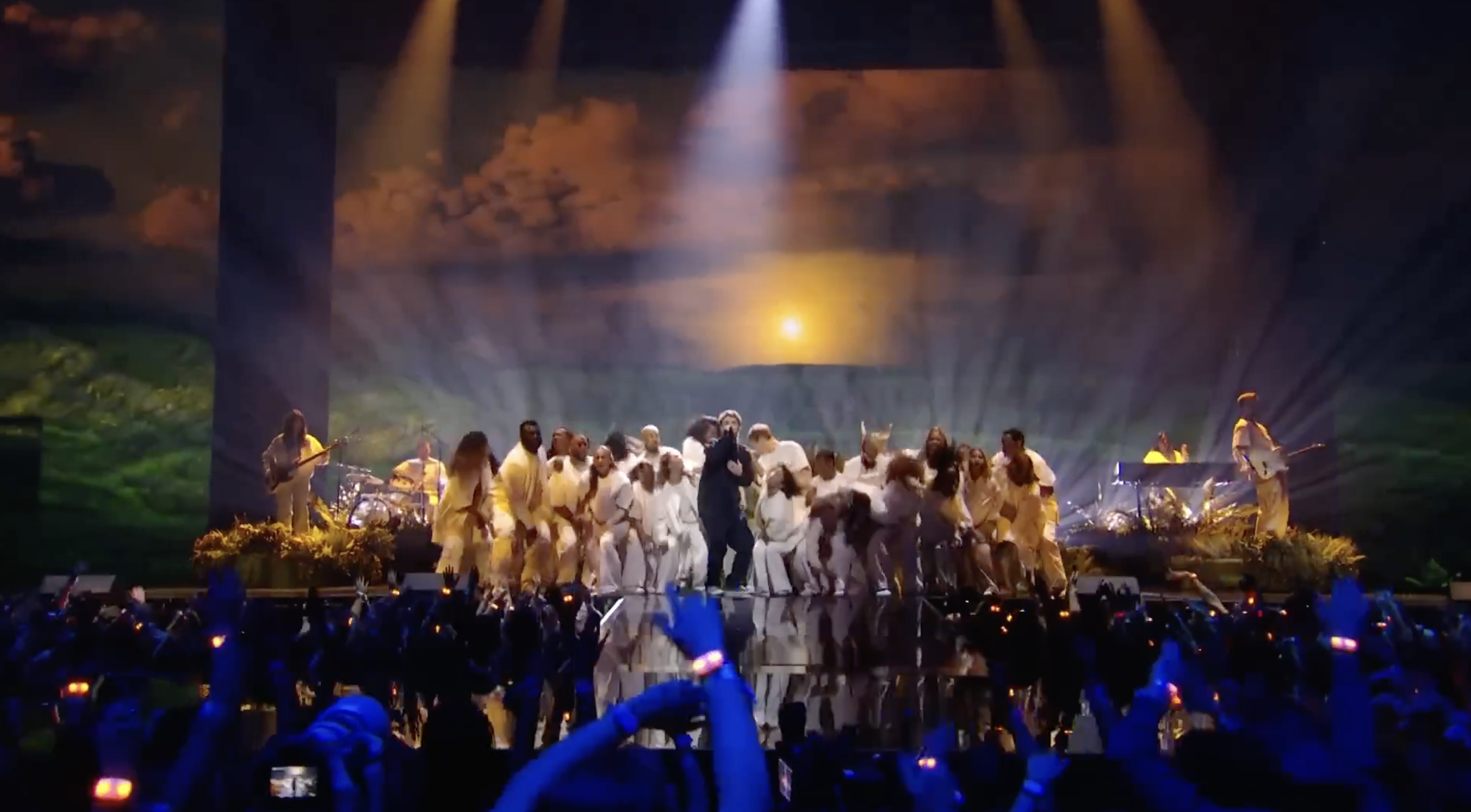 Large choir performing on stage with dramatic lighting and audience in background