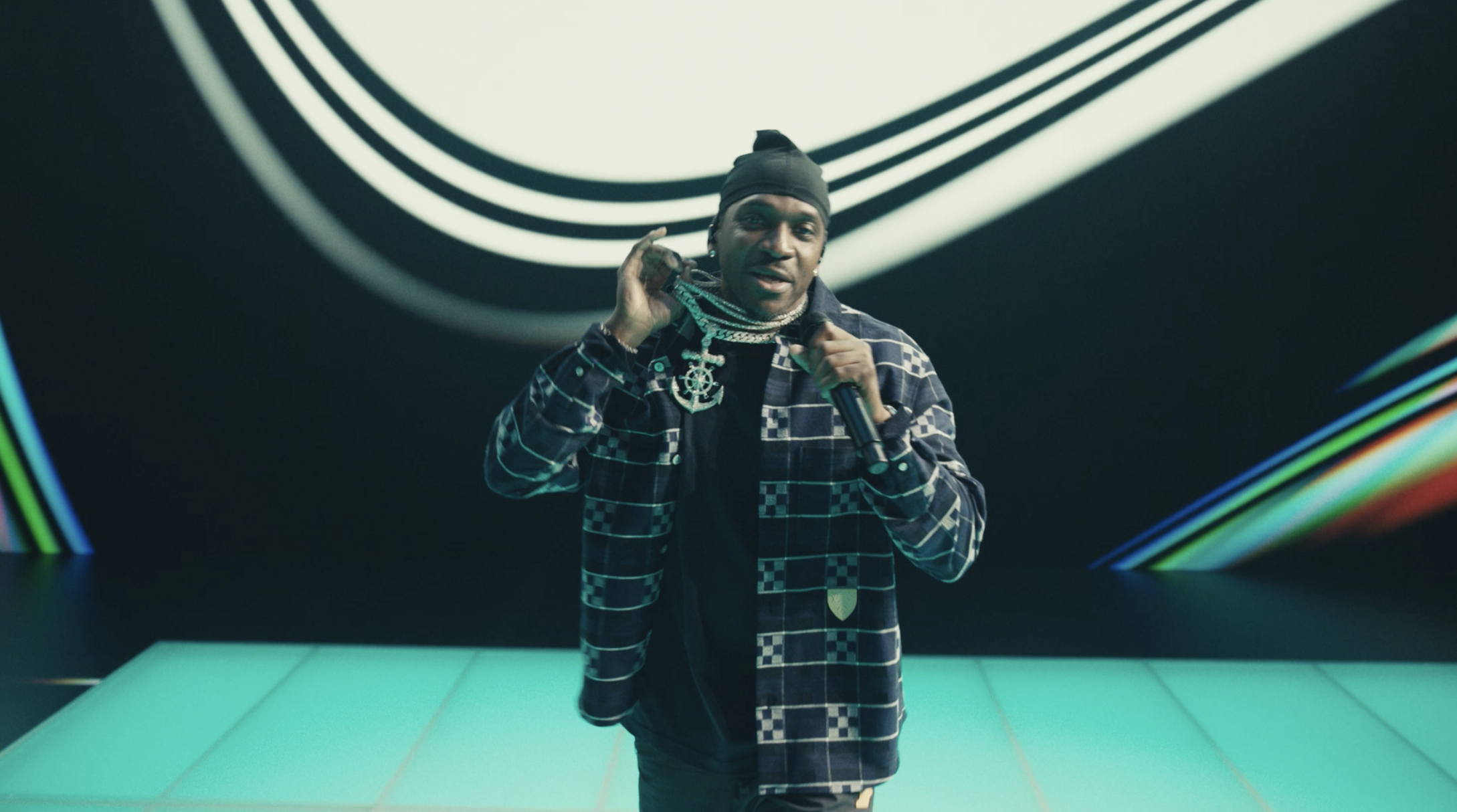 Performer in plaid jacket rapping on teal-gridded stage with curved backdrop