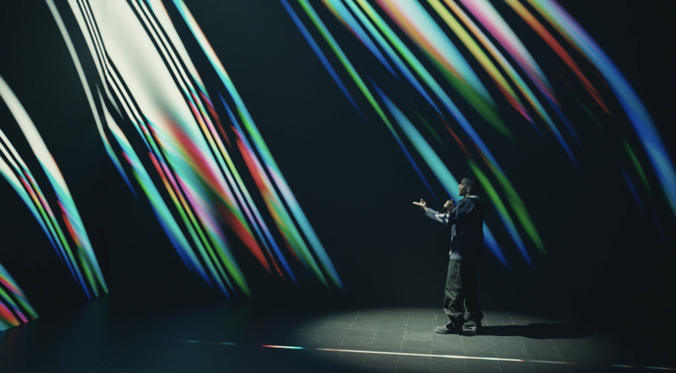 Person standing on stage with colorful light streaks in dark background