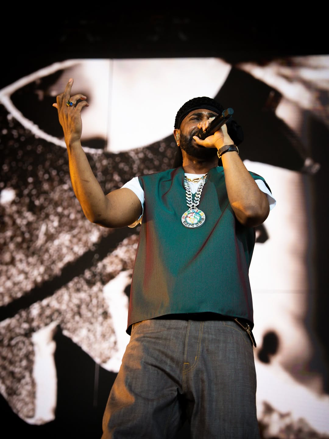 Rapper performing on stage with microphone, wearing teal shirt and chain