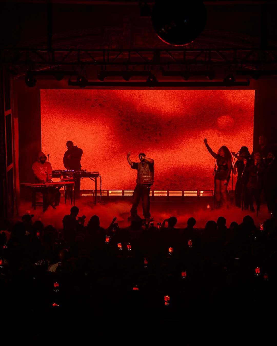 Concert stage bathed in intense red light with performers and audience