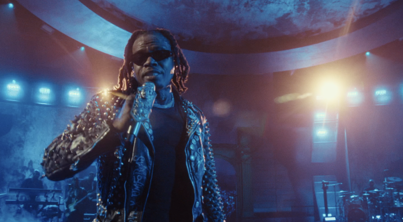 Musician performing on stage with dramatic blue lighting and studded jacket