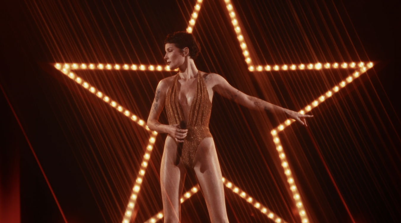 Performer in sparkling bodysuit posing dramatically in front of illuminated star