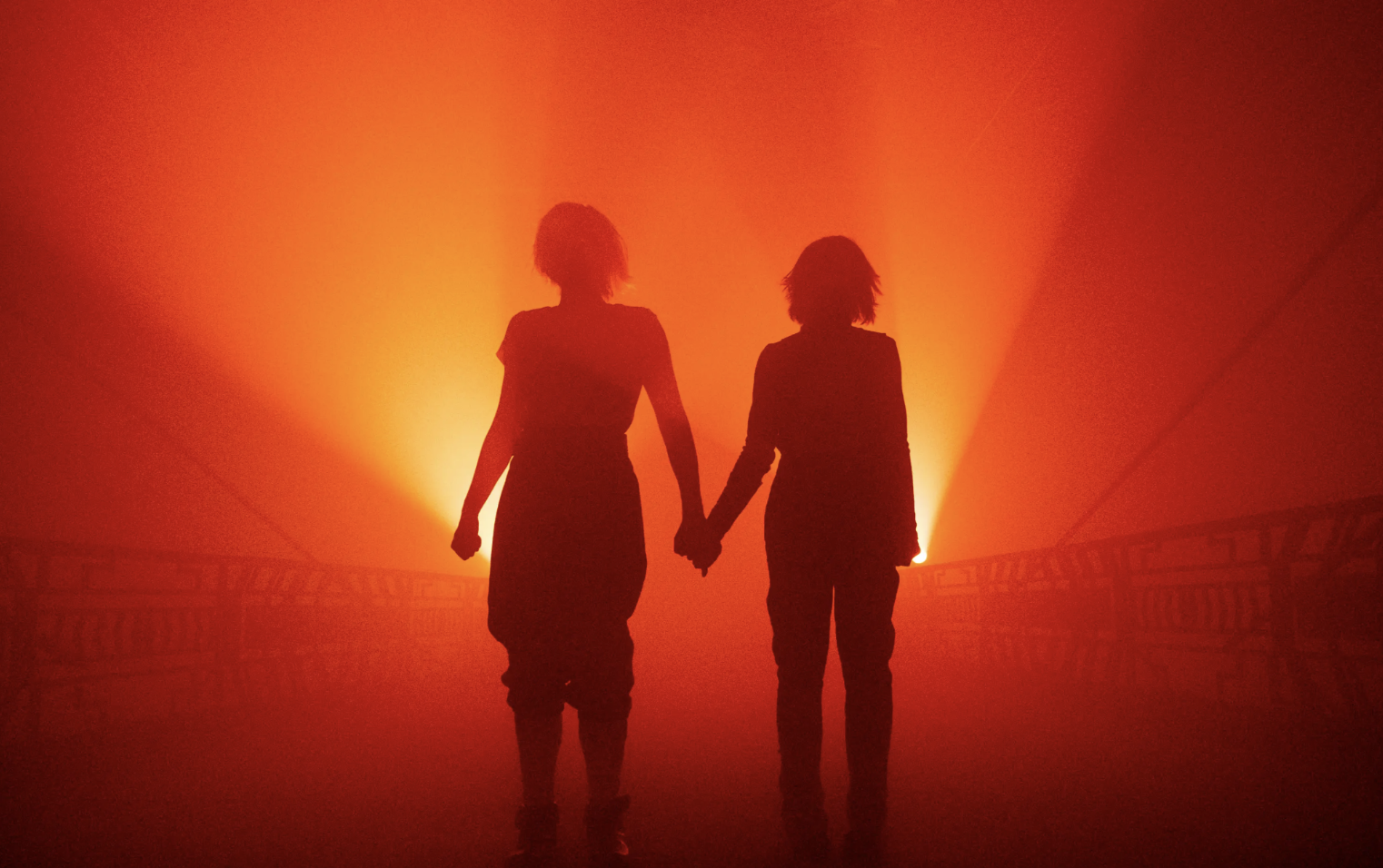Two silhouettes holding hands against vibrant red sunset backdrop