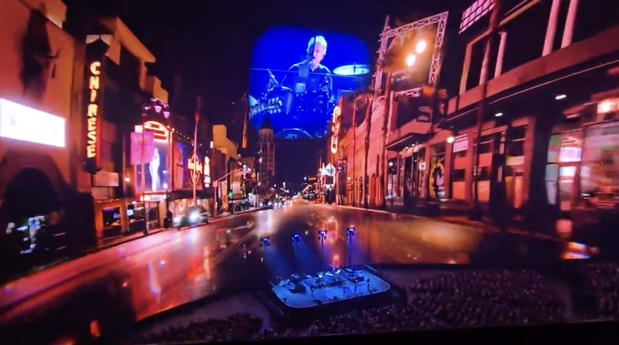 Drummer performing on large screen during concert on vibrant city street