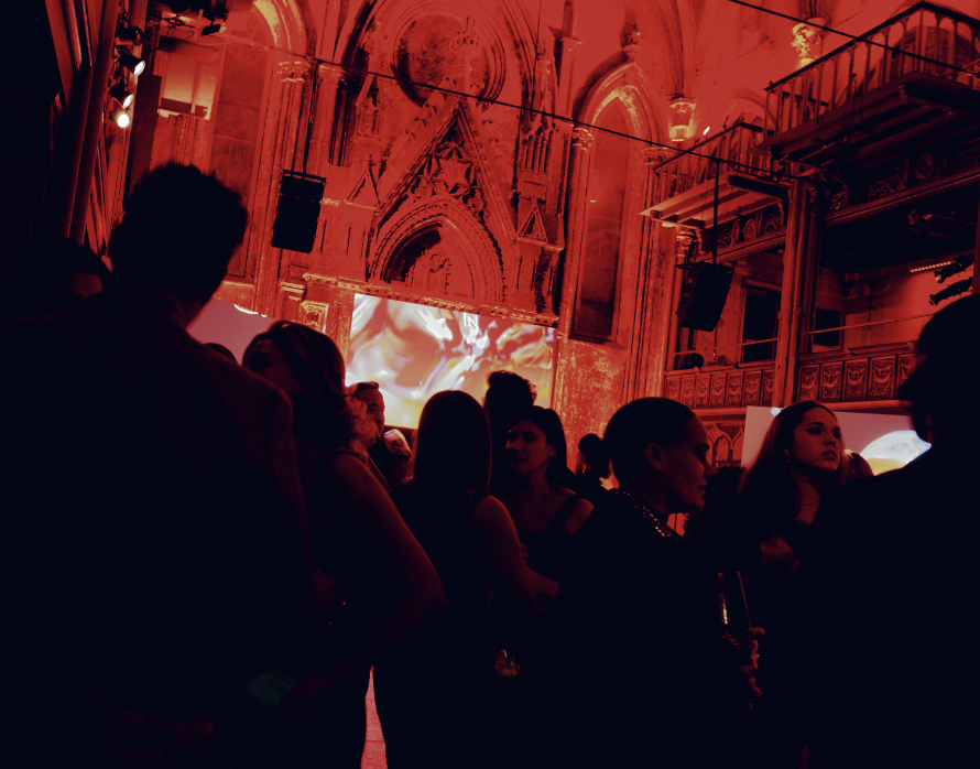 Crowded event with silhouettes in ornate red-tinted architectural venue
