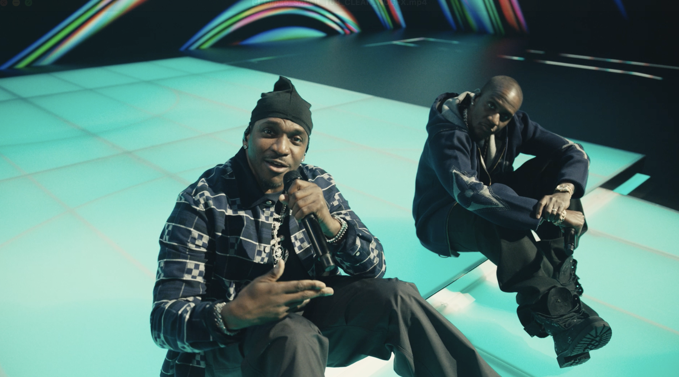 Two artists performing in futuristic blue-green studio with colorful light waves