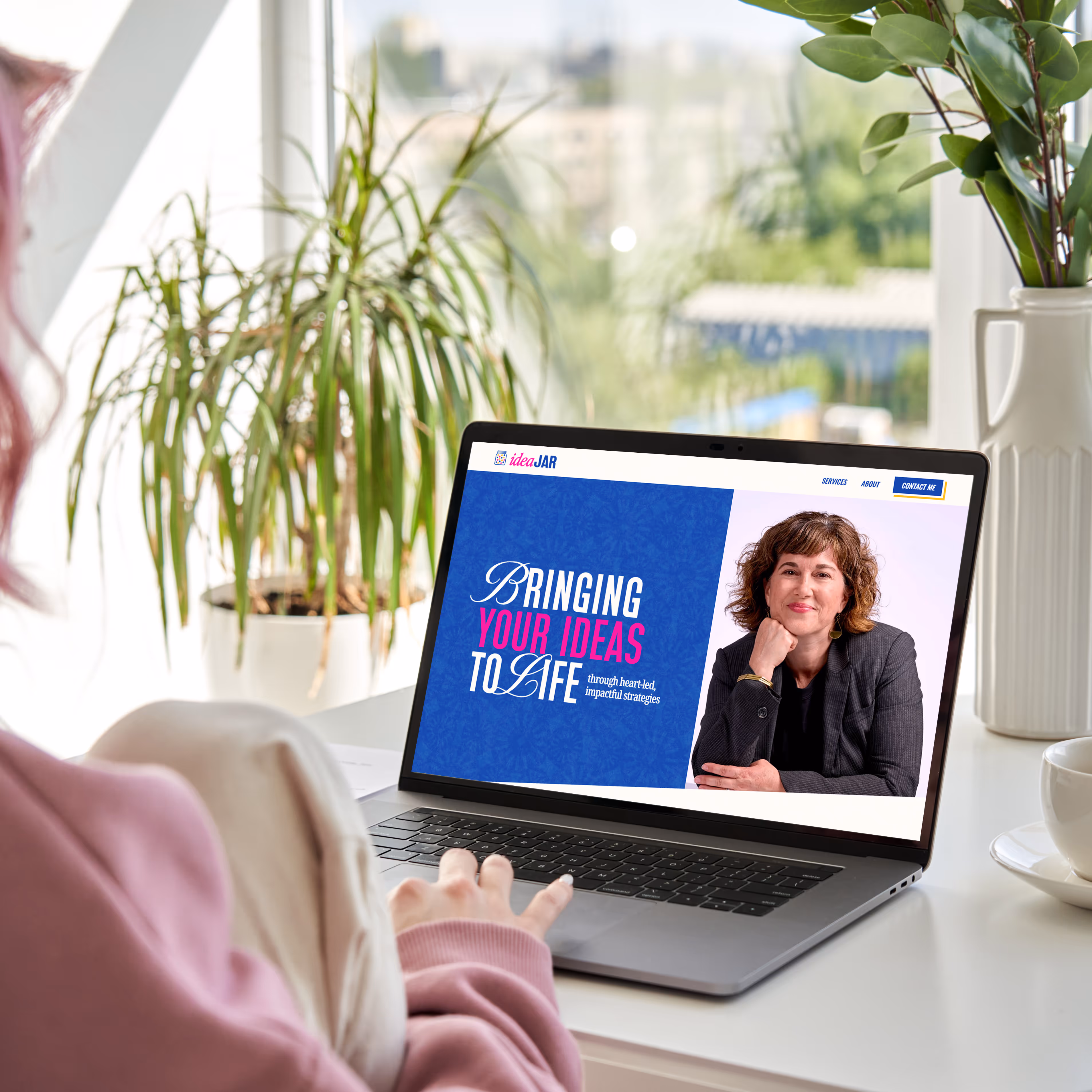 A woman is on her laptop looking at the new brand and website for Idea Jar Strategies created by EQBM Design Company.