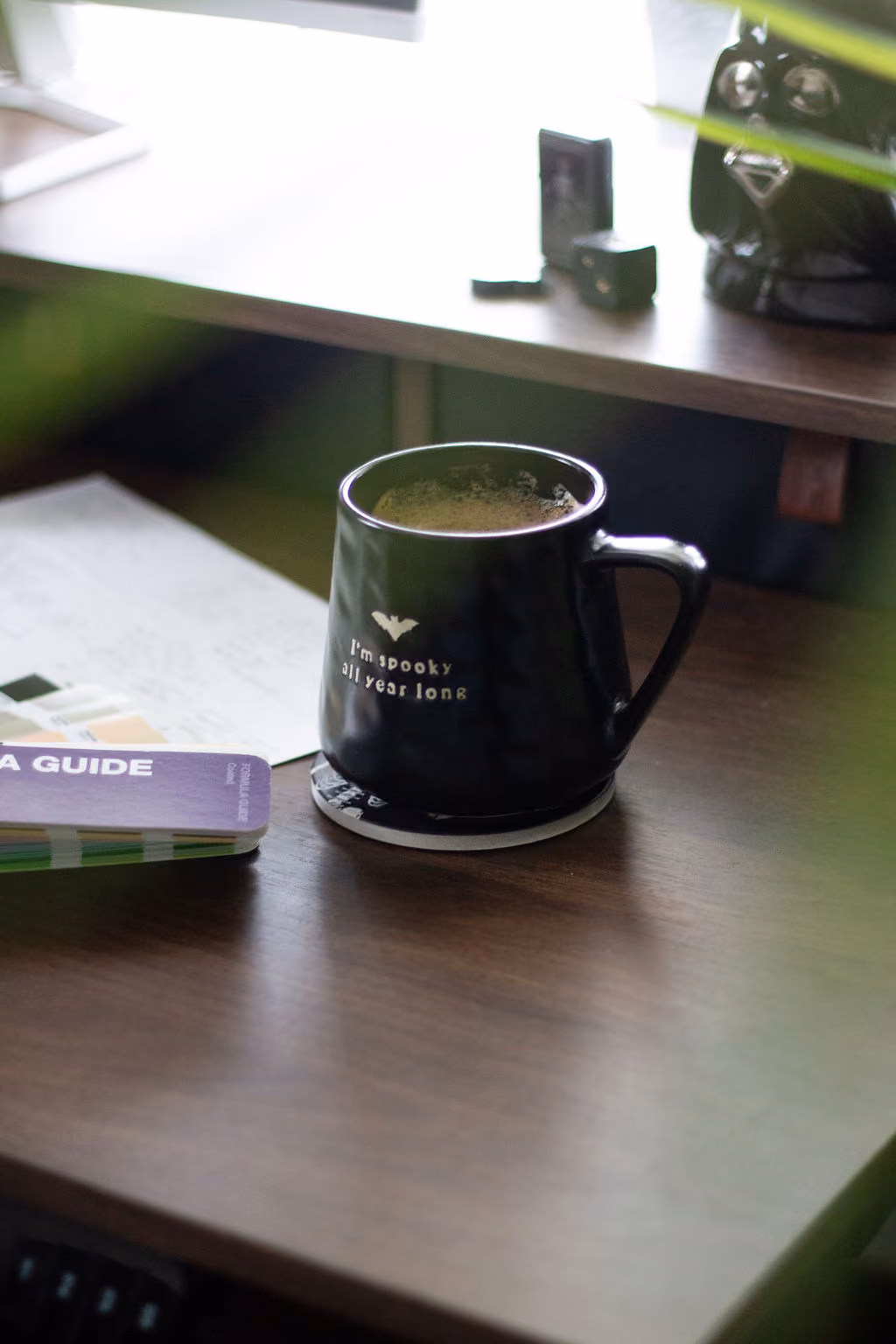 A black mug filled with coffee sitting on a desk for a graphic designer. The mug says "I'm spooky all year."