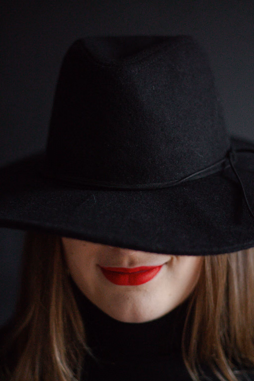 Hannah Hernandez wearing a wide brimmed black hat that covers the top part of her face and only shows her red lipstick.