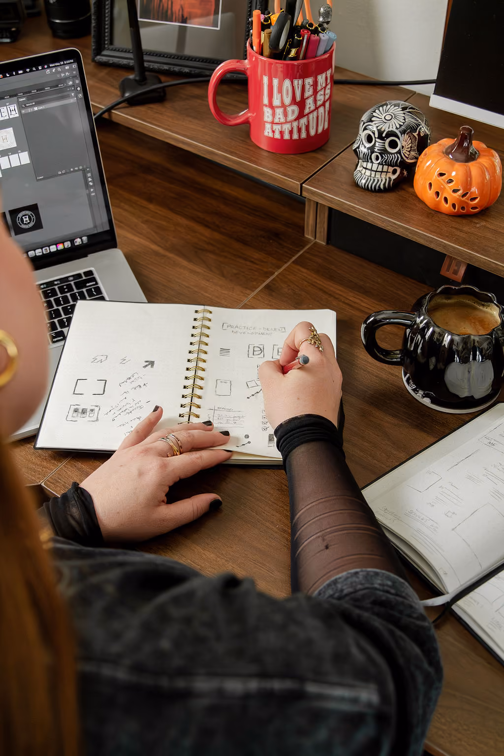 Hannah Hernandez is working at the desk in her studio. A notebook is open with the logo designs for a brand she is creating.