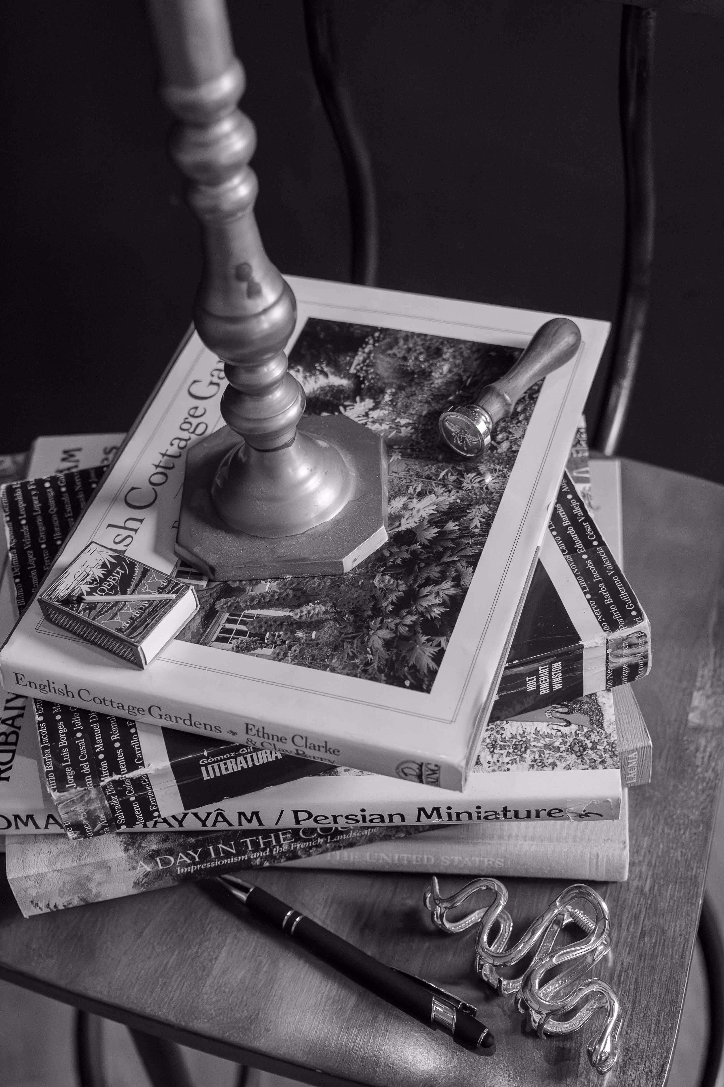 Stack of books on wooden chair with pen, snake-shaped hair clip, candle holder, and matchbox.