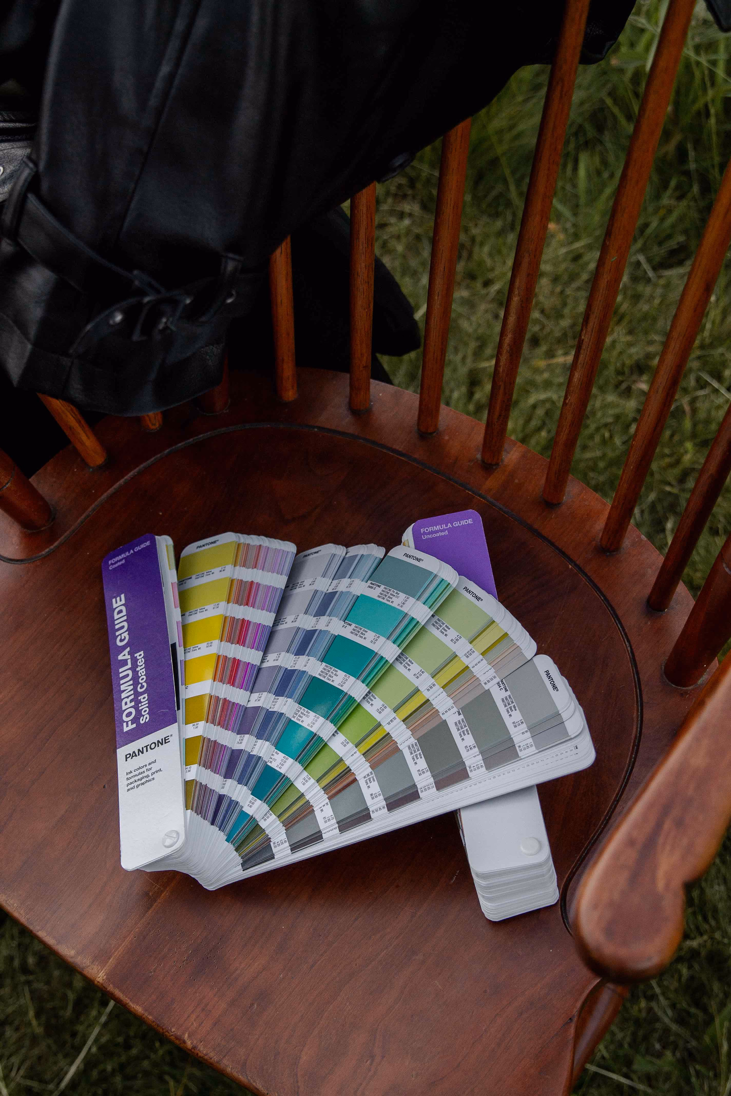Pantone Formula Guide color swatch fan with various shades laid open on a wooden chair seat.