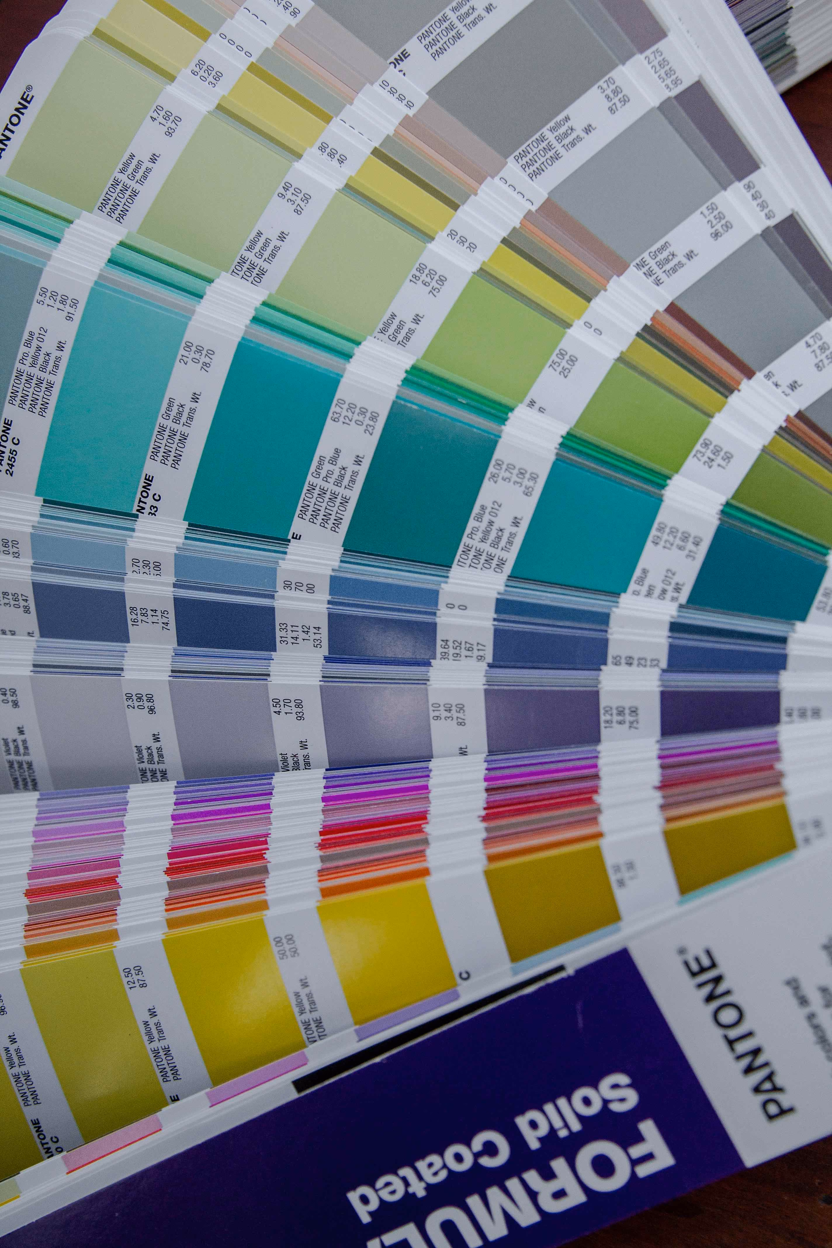 Fanned Pantone color swatch book showing a range of yellow, green, blue, violet, red, and orange shades.