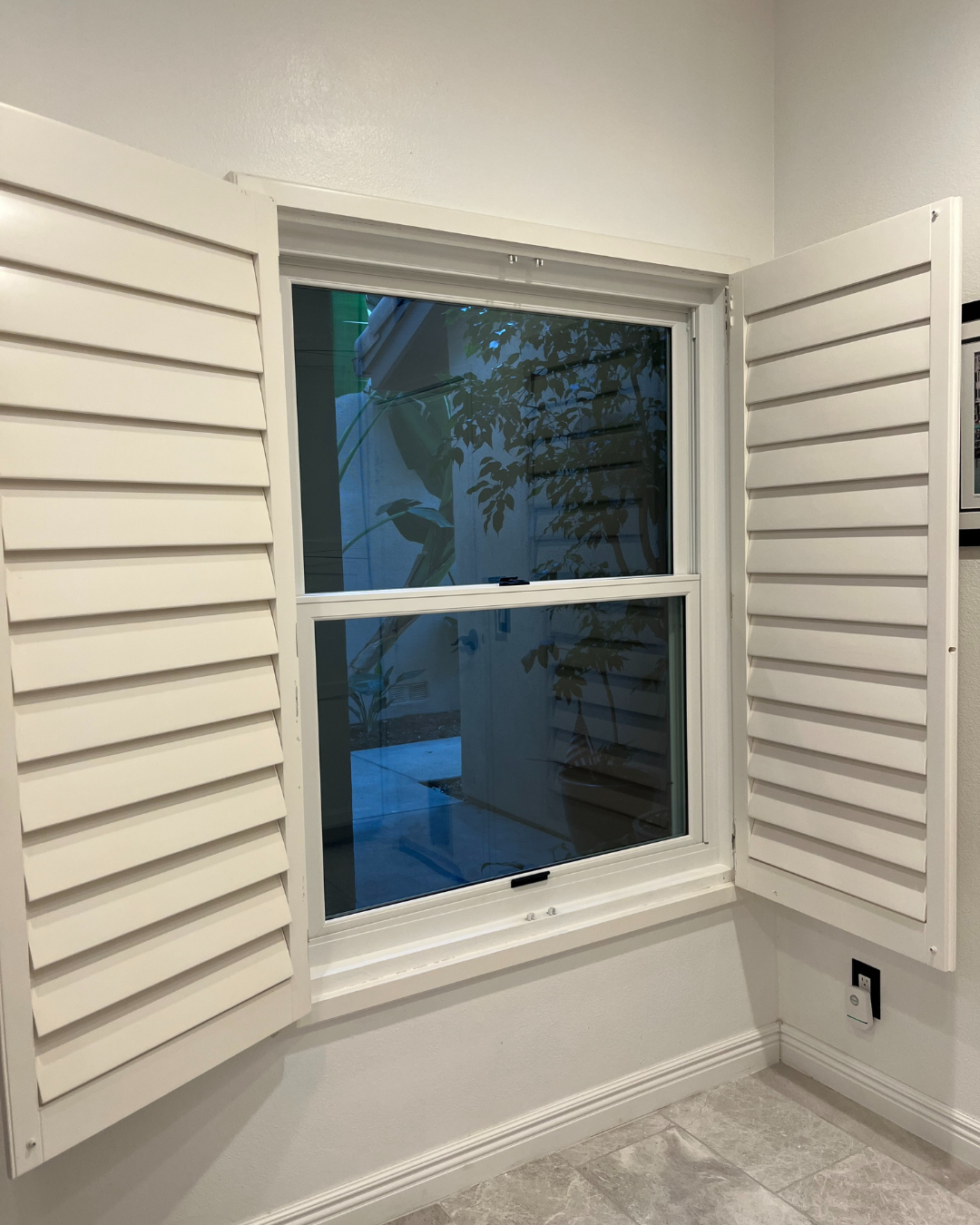 After: interior view of new sliding window without grid panes and open white exterior shutters