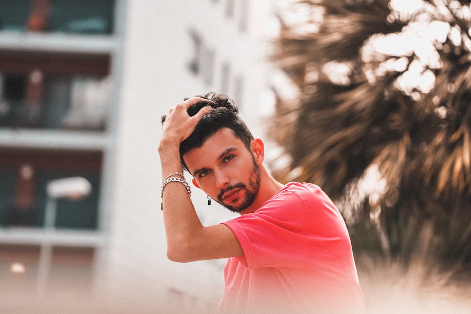 A confident man in a pink shirt poses outdoors with a thoughtful expression.