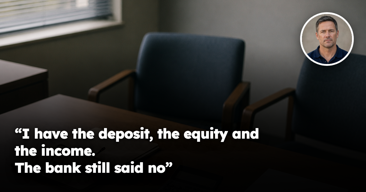 An empty loan officer’s desk in a suburban bank branch, with a closed manila loan application folder, reading glasses, a calculator with a blank display and two empty chairs pushed back on the far side of the desk.
