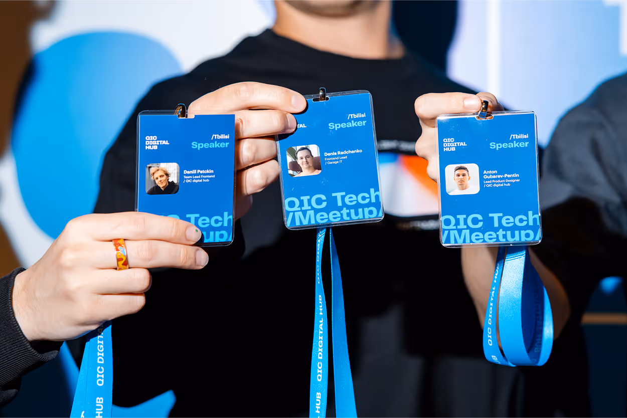 Three blue speaker badges for a QIC Tech Meetup held by QIC Digital Hub in Tbilisi, held up by a person.