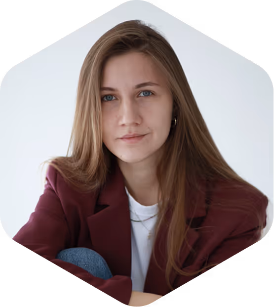Young woman with long light brown hair and blue eyes wearing a white shirt and maroon blazer sitting against a plain white background.