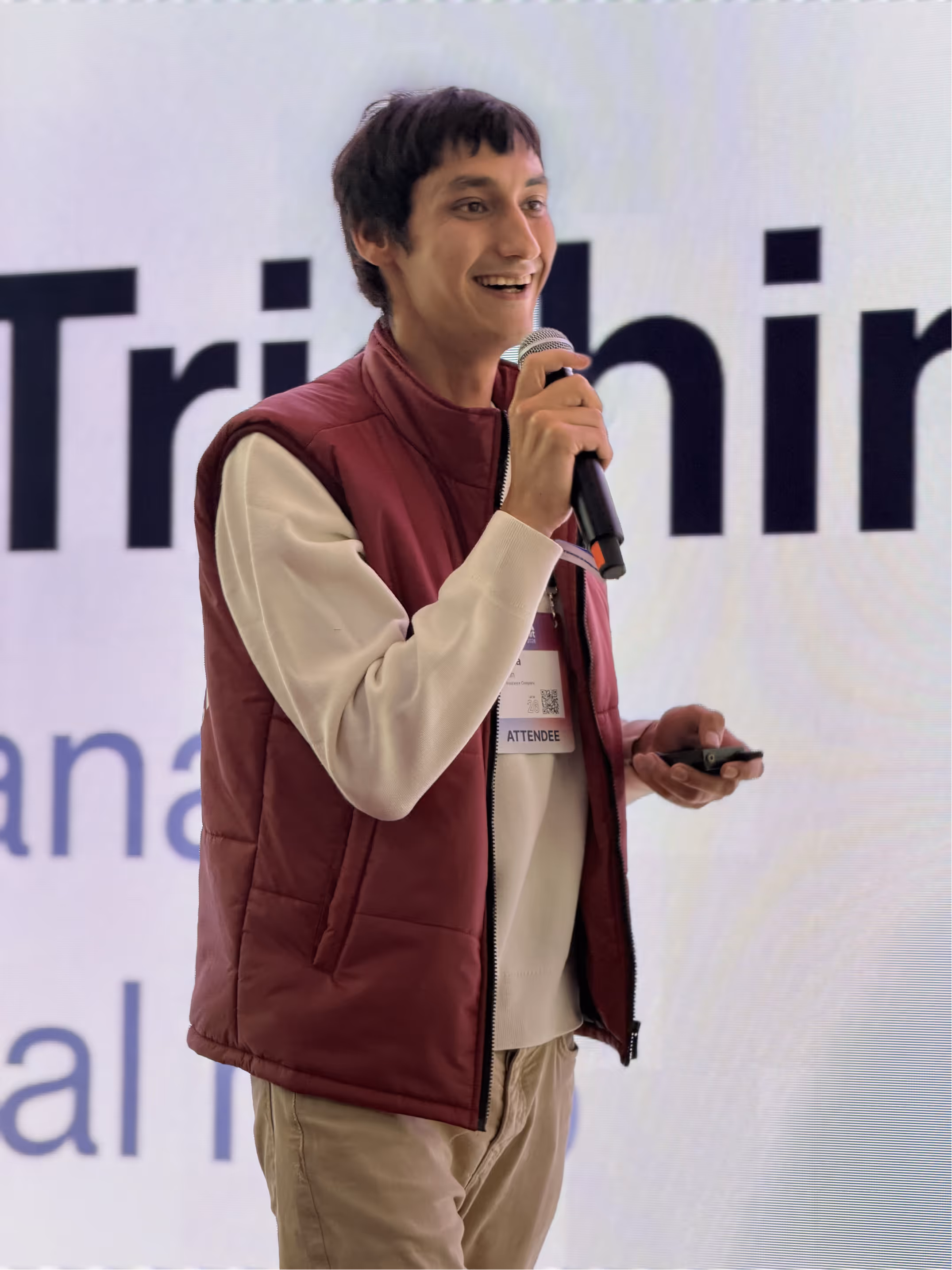 Smiling man in a maroon vest speaking into a microphone during a presentation.
