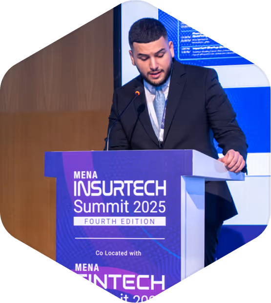 Man in a suit speaking at a podium during the MENA Insurtech Summit 2025 fourth edition.