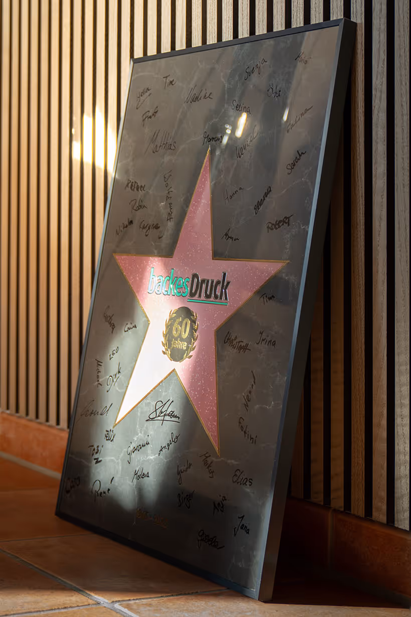 Gerahmtes Jubiläumsposter mit ‚60 Jahre backesDruck‘-Stern, signiert von Mitarbeitenden.