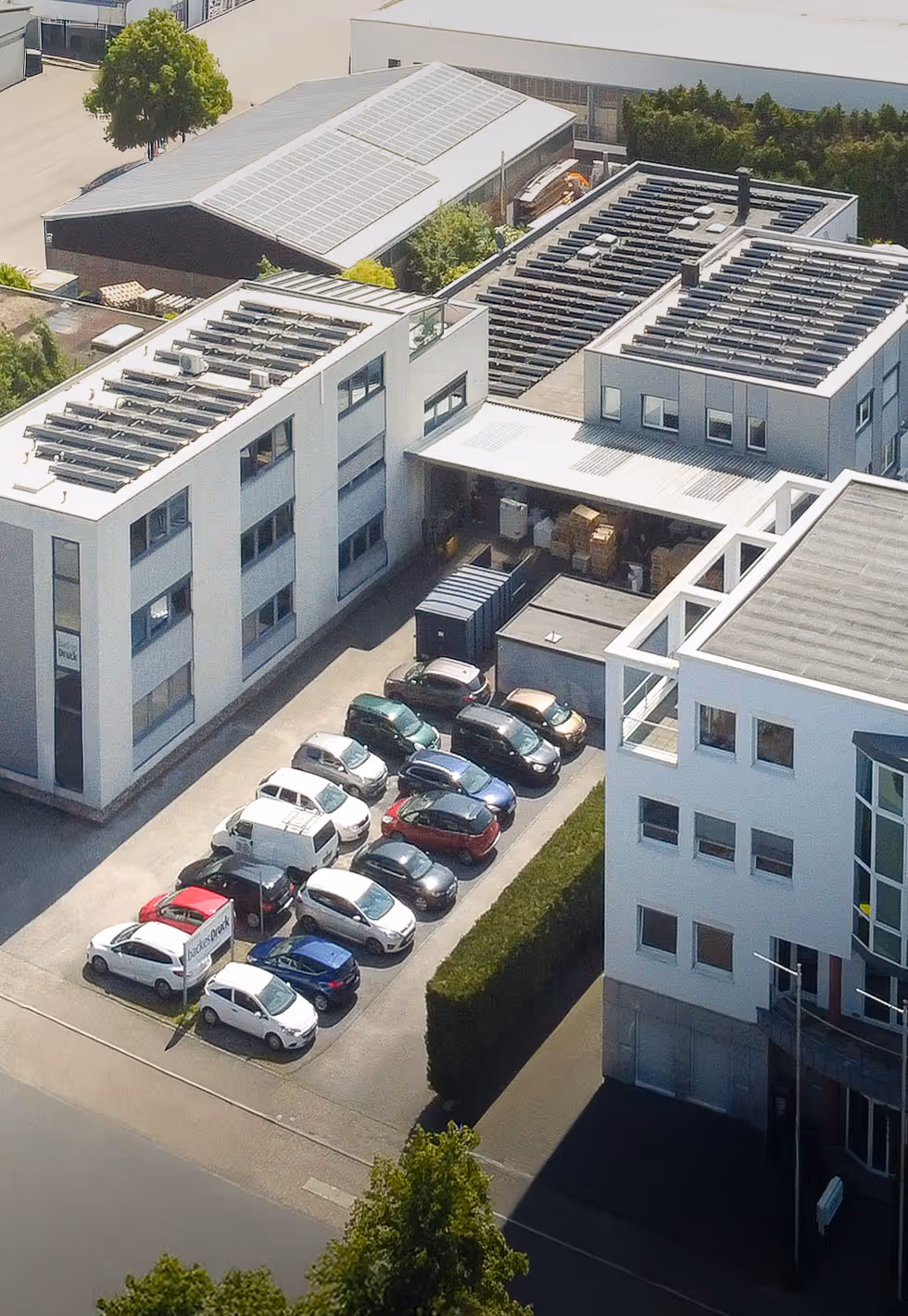 Eine Luftaufnahme des Gebäudes von backesDruck mit einer großen Photovoltaik-Anlage auf dem Dach und parkenden Autos davor.