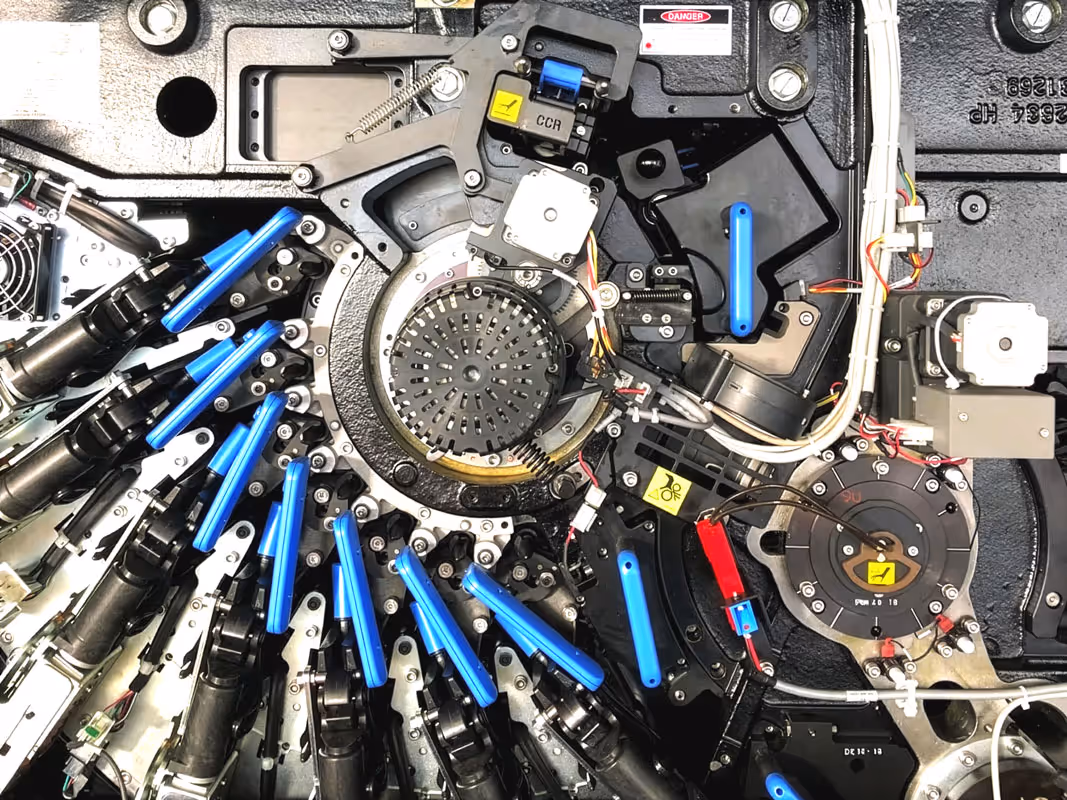 Innenansicht der HP Indigo 6900 Digitaldruckmaschine: Farbstationen mit blauen Griffen rund um den zentralen Druckzylinder, Hightech-Komponenten und präzise Steuerungstechnik.