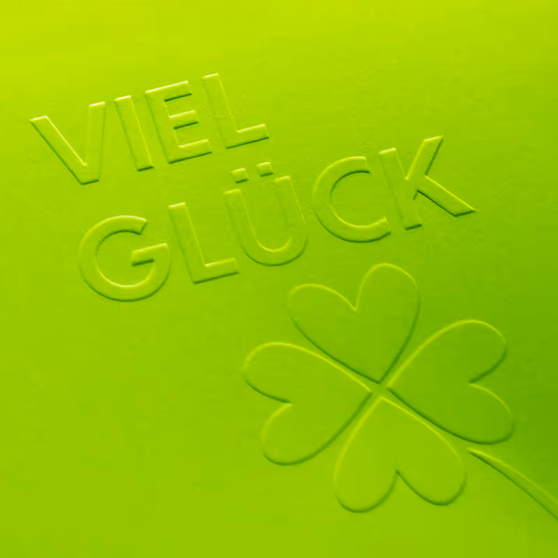 Neongrünes Druckmuster mit fühlbarer Reliefprägung – plastisch geprägte Schrift und Klee-Symbol für markante Haptik.